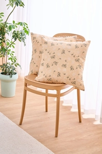 Set of 2 beige floral pillow covers with black flower branch prints on a rattan chair