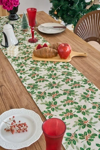 Close-up of Christmas table runner with holly leaves and red berries on wooden table