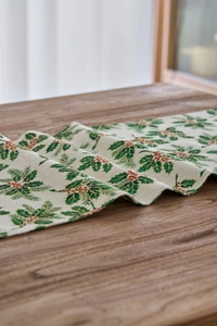 Close-up of Christmas table runner with green holly leaves and red berries pattern