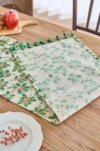 Close-up of Christmas table runner with green holly leaves and red berry print with tassels