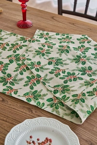 Detailed close-up of Christmas table runner with holly leaves on rustic wooden table