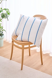 Detail view of white cushion cover with blue embroidered stripes on a rattan chair
