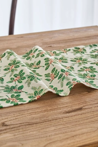 Close-up of festive table runner with holly leaves and red berries on cotton linen fabric