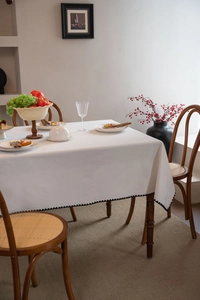 Detail view of white tablecloth with black scalloped embroidery on a dark wooden table