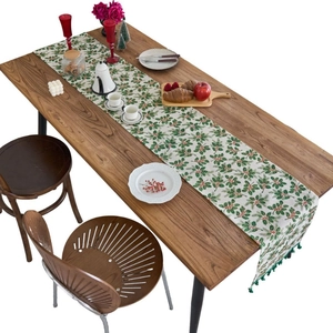 Christmas table runner with holly leaf print and green pom-poms on dark wood table