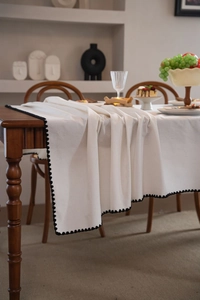 Close-up of white linen tablecloth with black pom-pom trim draped on a wooden table