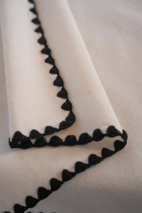 Detail of scalloped black stitched edges on natural beige linen cotton tablecloth