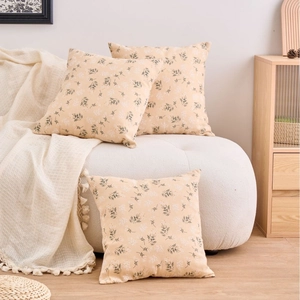 Three square cream cushion covers with green floral pattern on a cozy fabric sofa