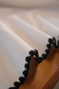 Detailed macro view of white cotton linen fabric with intricate black crochet lace edges