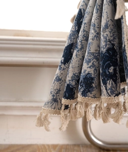 Detail of blue and white floral jacquard fabric with elegant cream cotton fringe tassels