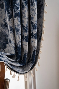 Detail view of blue and white floral jacquard curtain with elegant off-white tassel trim