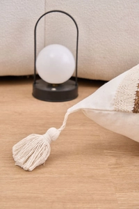 Detailed close-up of decorative fringe and boho woven texture on cream throw pillow