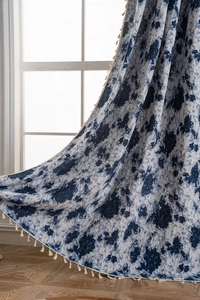 Close-up of blue floral jacquard curtain with off-white fringe tassels on wood floor