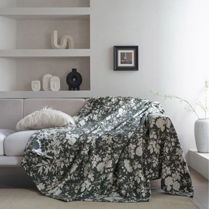 Floral dark green throw blanket with white leaf patterns on a soft cream sofa