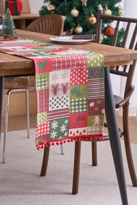 Close-up of Christmas table runner with reindeer motifs and red pom-pom fringe detail