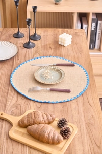 Detail of round woven jute placemat with vibrant blue crochet wave border on a wooden table