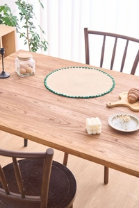 Detail of round jute placemat with green scalloped edges on a rustic wooden dining table