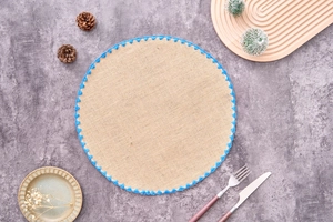 Detailed top view of a round jute placemat with blue crochet wavy lace on stone background