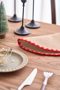Detalle de mantel individual de yute con borde festoneado rojo en mesa de madera