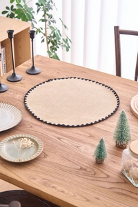 Detail of round woven placemat with natural texture and black wavy lace border decor