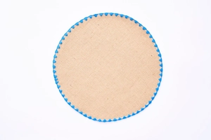 Close-up of circular jute placemat with decorative blue woven lace edge on white background