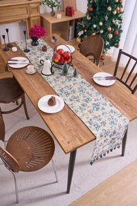 Detailed view of floral table runner with colorful tassels on a wooden dining table