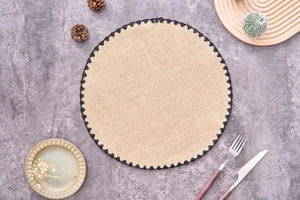Detail of round cotton yarn placemat with black zigzag lace edge on a stone surface