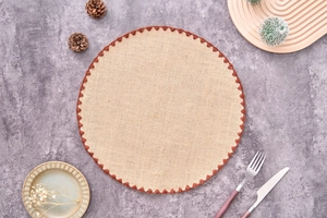 Detail showing natural jute round placemat with brown scalloped trim on textured surface