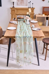 Detail of light green sheer lace table runner with colorful floral embroidery on wood