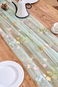 Close-up of light green lace table runner with multi-colored floral and butterfly embroidery