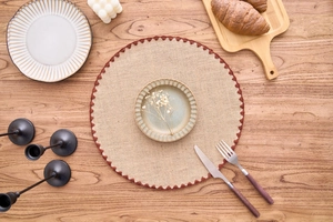 Detail of round woven cotton placemat with dark scalloped edges on a wooden table