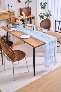 Detail of light blue lace table runner with floral embroidery on wooden dining table