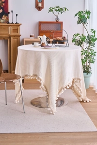 Detail of creamy white waffle weave tablecloth with decorative fringe tassels on a round table