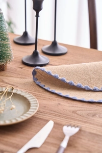 Close-up of rustic jute placemat with blue crochet lace edge on a wooden table