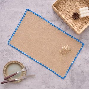 Détail du set de table rectangulaire en jute avec broderie festonnée bleue sur les bords