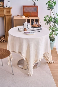 Detail of waffle weave pattern cream tablecloth with decorative fringe edges on a round table