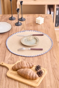Detail of round cotton braided placemat with blue woven lace edge on wooden table