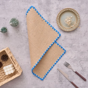 Détail du set de table en jute naturelle avec broderie bleue et bords ondulés élégants