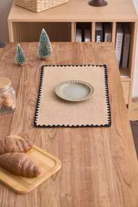 Gros plan du set de table en jute tressé avec broderie noire sur table en bois