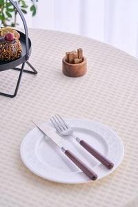 Detail of waffle weave cream tablecloth with a decorative white plate and rustic cutlery