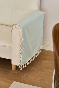 Detail of light blue waterproof fabric with cream tassels draped over a sofa armrest