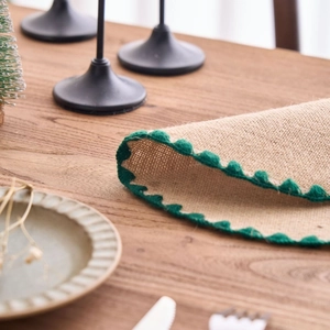 French country style jute placemat with green pompom trim on a rustic wooden table
