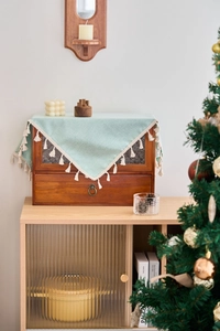 Close-up of mint green textured tablecloth with cream tassels on a vintage wooden cabinet