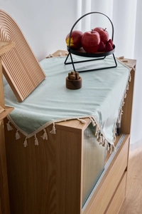Detail of mint green TPU tablecloth featuring elegant cream tassels on a wooden cabinet