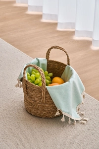 Close-up of woven seagrass storage basket with green tassel fabric and fresh fruit decor