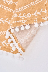 Detalle de la funda antipolvo de lino y algodón amarillo con flores y pompones blancos