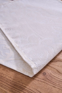 Close-up of cream damascus jacquard table runner fabric with floral pattern on wood surface