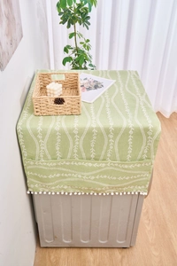 Detalle de la funda antipolvo floral verde con flecos de pompones y bolsillos laterales