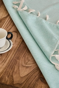 Close-up of mint green waterproof tablecloth with weave texture and tassel edge on wood
