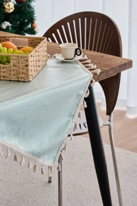 Close-up of mint green waterproof tablecloth with woven tassel fringe on wooden table